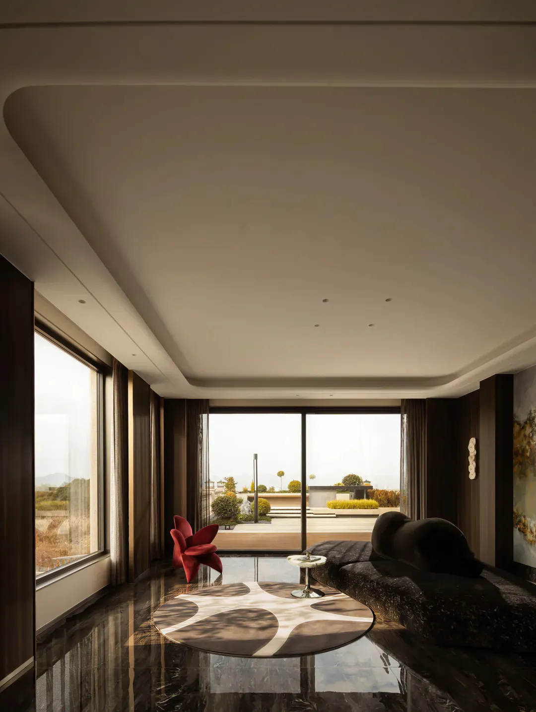 Modern luxury living room featuring glossy black marble flooring, a sculptural red chair, a dark curved sofa, circular patterned rug, and large floor-to-ceiling windows overlooking a landscaped terrace.