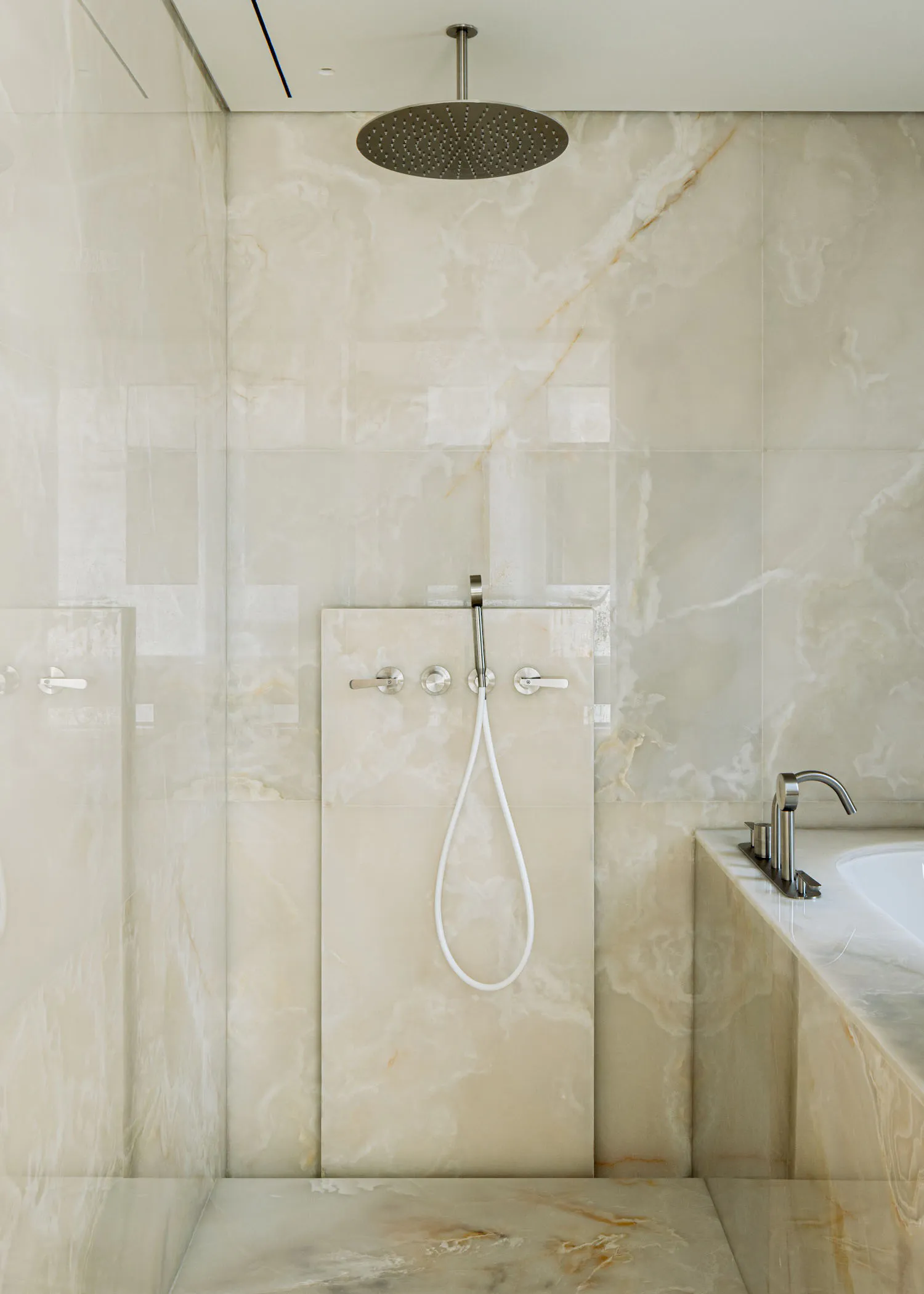 Modern luxury bathroom with large round stainless steel rain shower head, white handheld wand, chrome fixtures, and full-height Calacatta marble walls and floor.