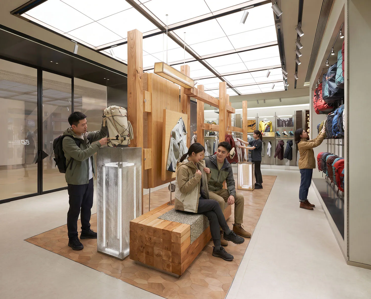 Modern retail interior of an outdoor gear store featuring a large modular wooden display structure with metal mesh lighting columns and customers browsing merchandise.