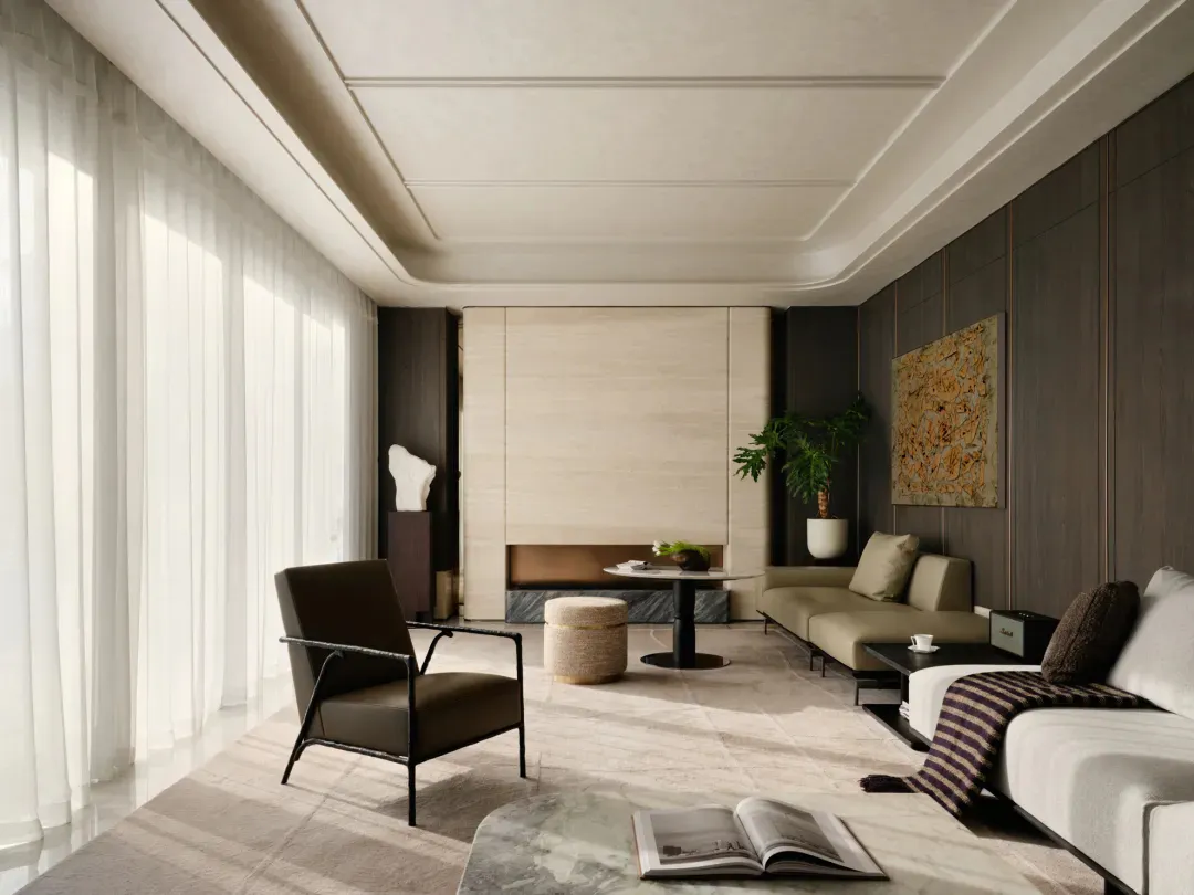 Modern luxury living room featuring dark wood paneling, a light wood accent wall with fireplace, beige sofa, brown leather armchair, round coffee table, and large abstract artwork, illuminated by natural light from floor-to-ceiling sheer curtains.
