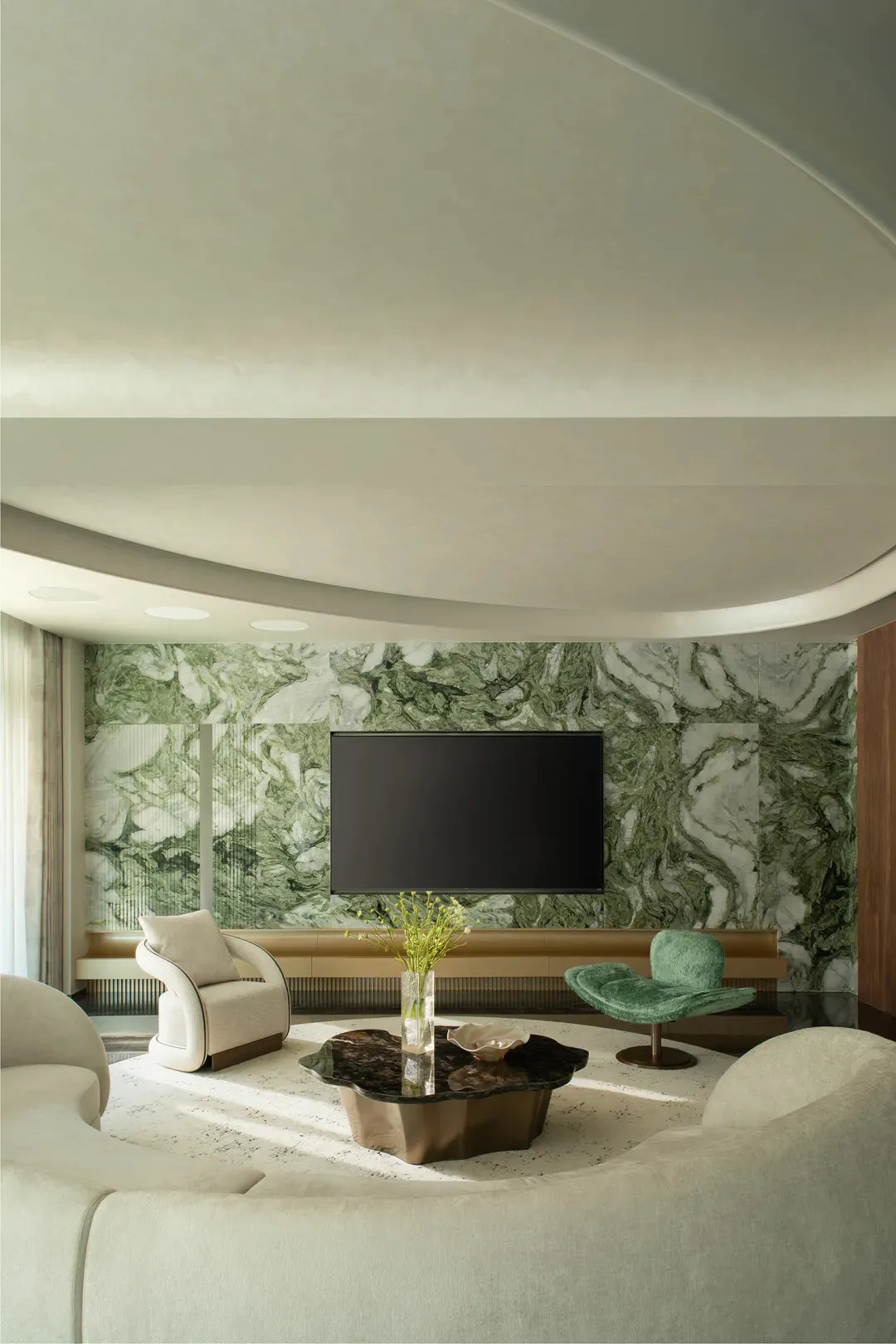 Modern luxury living room featuring a large curved ceiling, green marble accent wall with mounted TV, cream curved sofas, a green velvet swivel chair, and an irregular dark stone coffee table on a light rug.