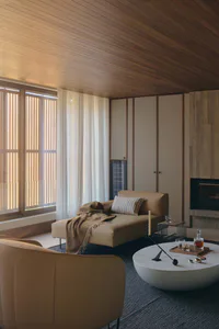 Modern living room interior with wood-paneled ceiling and walls, a tan leather chaise lounge with a checkered pillow and knitted throw, a round white marble coffee table with drinks and decor, and large windows with sheer curtains.