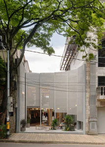 台北現代精品店店面，以大面積半透明白色簾幕為立面，搭配戶外座位、盆栽植物，店內可見服裝展示架，四周環繞茂密綠樹。