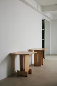 Two minimalist solid oak console tables with T-shaped legs placed in an empty industrial loft with raw concrete walls and floor.