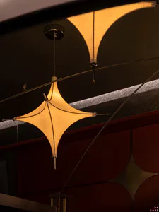 Close-up view of a star-shaped fabric pendant lamp with warm glowing light, suspended from a dark ceiling with geometric red and gold architectural details.