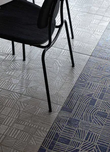 Close-up view of two different patterned ceramic floor tiles in grey and deep blue, with the legs and seat of a black metal chair resting on the grey section.
