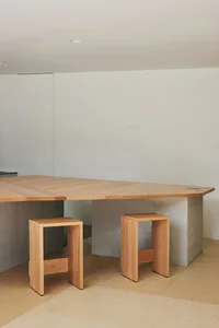 明亮極簡風室內空間中，L型的實木橡木餐桌搭配厚實混凝土支撐，以及兩張同材質的橡木矮凳。
