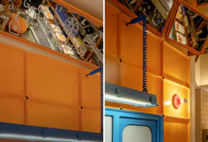 Close-up view of a vibrant orange modular wall system with blue coiled cords, retro fluorescent lighting, and mirrored menu signage in a bagel shop.