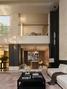 Modern luxury double-height living room with travertine stone walls, white sectional sofa, black coffee table, and upper mezzanine level overlooking the space.