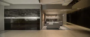 Modern minimalist coffee shop interior with a large grey stone counter, dark stacked tile feature wall with illuminated signage reading 'mo labo coffee', light wood flooring, and recessed lighting.