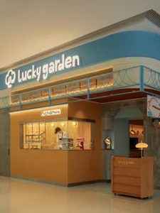 名為幸運花園的現代商業義大利麵小站，採用溫暖橙色木質板材、藍色弧形天花板，發光的展示窗內可見廚師與紅色攪拌機，前方設有木質迎賓台。