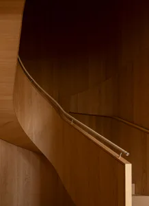 Close-up view of a curved wooden staircase made of warm oak with a beaded handrail and glass panel.