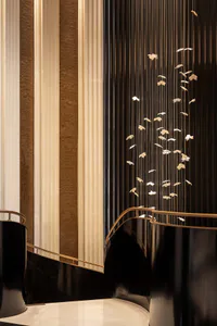 Luxurious curved staircase with glossy black balustrade and brass handrail, featuring an artistic installation of golden butterflies suspended on fine vertical strands against a dark background, next to tall beige curtains and a brown tiled wall.