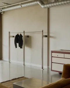 Modern minimalist entryway featuring a freestanding stainless steel clothing rack with black jackets, a dusty rose and light wood console cabinet, polished concrete floor, and exposed galvanized ductwork.
