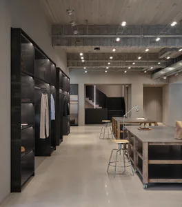 Modern industrial minimalist dressing room with black steel open wardrobes, concrete floor, wooden work tables on wheels, and exposed ceiling infrastructure.