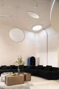 Modern living room featuring a sculptural white curved ceiling, large circular pendant lights, a long black velvet sectional sofa, metallic coffee tables, and a blue arched shelving unit in the background.
