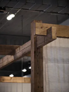 Close-up of a heavy reclaimed wooden beam with traditional joinery details in an industrial-style loft space, with concrete ceiling and track lighting in the background.