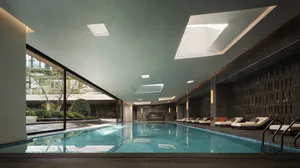 Modern indoor swimming pool in a luxury spa with dark textured stone walls, multiple skylights, and lounge chairs along the side.