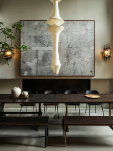 Modern minimalist dining room featuring a long dark wood table, wooden benches, black dining chairs, a large abstract concrete artwork on the wall, a tall sculptural white paper pendant lamp, and warm wall sconces.