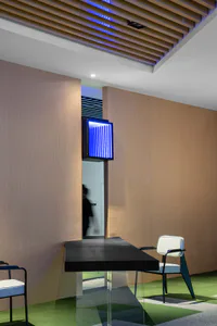 Modern office reception area with a black floating desk on clear acrylic legs, white and black chairs, wood panel walls, green patterned carpet, and a glowing blue vertical light fixture mounted on the wall.