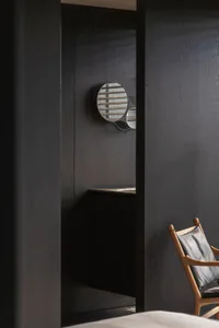 A modern dark wood entryway featuring a unique circular mirror shaped like a tennis racket, a wooden sling chair with black leather, and built-in cabinetry.