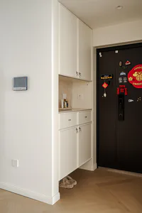 Modern minimalist white entryway cabinet with upper storage, drawers, and open shelf next to a black front door decorated with magnets and Chinese wedding decorations.