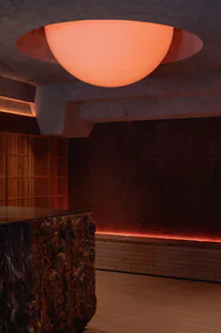 Modern cave-inspired bar lounge featuring a large glowing orange spherical pendant light, dark textured volcanic walls, a rough-hewn marble bar counter, wooden cabinetry, and warm ambient lighting.