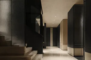 Modern luxury hallway with black textured wall panels, light marble staircase, and polished marble floor leading to a distant doorway.
