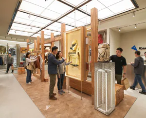 現代戶外用品零售店內部，設有木質結構框架、網狀金屬展示塔，以及顧客正在觀看明亮照明的黃色雨衣展示。