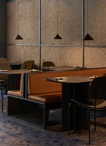 Modern Japanese-style restaurant interior with brown cork tile walls, burnt orange leather booth seating, dark wood tables, and pendant lights over a patterned blue and brown carpet.
