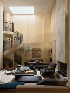 Luxurious double-height living room featuring travertine marble walls, a dramatic spiral staircase, layered neutral seating, and a large skylight.