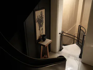 View of a modern curved staircase with black metal railing, light marble floor, oak console table, and large framed botanical wall art on a dark wall.