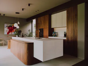 Modern kitchen featuring a large walnut wood island with a light concrete countertop, integrated sink, turquoise stand mixer, wooden cabinetry, and abstract painting in the background.