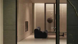 View into a modern minimalist living room featuring travertine walls, a sculptural black velvet sofa, a suspended woven spherical sculpture, and warm ambient lighting.
