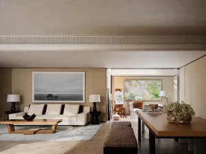 Modern minimalist living room with white sofa, large seascape painting, wooden coffee table, and adjacent dining area with large floral arrangement.