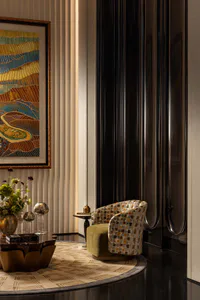 Elegant modern interior corner featuring a green velvet and multicolored mosaic patterned swivel armchair, abstract landscape painting, dark fluted wall panel, and sculptural coffee table on a geometric rug.