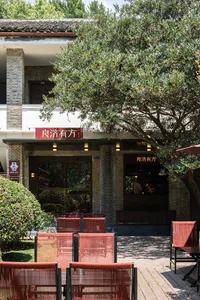 Outdoor seating area of a heritage building with red rope-weave chairs on a wooden deck, surrounded by lush greenery and a large tree, with Chinese signage reading 良濟有方.