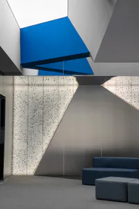 Modern corporate lobby interior featuring a large backlit wall with white circuit board patterns, angular blue ceiling panels, and blue modular seating on grey carpet.
