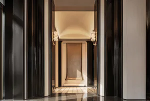 Symmetrical luxury hallway featuring dark fluted marble walls, light stone archway, and matching wall sconces with glowing spherical lights.