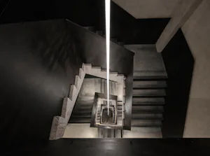 Looking down into a dramatic concrete spiral staircase with a powerful vertical linear light fixture descending through the center of the void.