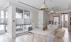 Modern minimalist dining room with white walls, light wood flooring, a rectangular dining table, upholstered chairs, and an open kitchen with light wood cabinetry in the background.