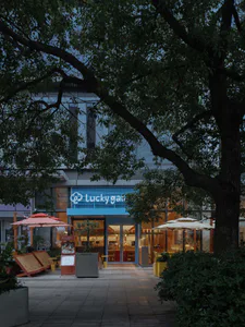 現代咖啡廳店面，藍色發光招牌寫著Lucky Garden，玻璃入口大門、戶外遮陽傘，以及黃昏時的茂密樹木。