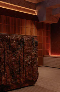 A large, rough-textured reddish-brown natural stone reception desk in the foreground with warm wooden cabinetry and dramatic cove lighting in the background.