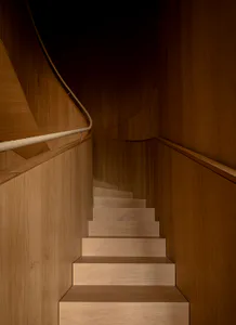 View looking down a curved wooden staircase made of light oak with a thick rope handrail mounted on a wooden wall.