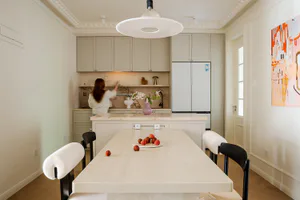 Modern open kitchen and dining area featuring a large Calacatta marble island and dining table, soft beige cabinetry, and a woman arranging flowers in the background.