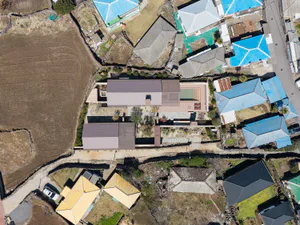 Aerial photograph of a modern single-story villa with a purple metal roof, rectangular swimming pool, and landscaped courtyard, situated among traditional houses with blue and yellow roofs in a rural Taiwanese setting.