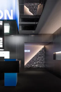 Modern luxury retail interior featuring dark grey walls, blue accent lighting, and a large crinkled metallic sculptural wall with illuminated brand signage.