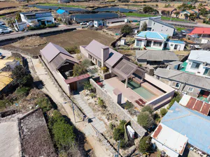 Aerial photograph of a modern single-story courtyard villa featuring pinkish stone walls, a rectangular swimming pool, large overhanging roofs with solar panels, and surrounding farmland in Taiwan.