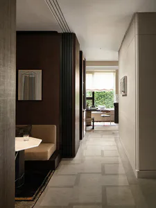 Modern interior hallway with dark walnut wood paneling, a built-in beige banquette with marble table, geometric patterned stone floor, and a view to a bright window seat at the end.