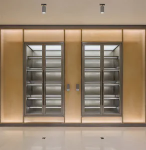 Modern built-in double wine cellar with stainless steel glass doors, internal LED lighting, and warm backlit onyx or stone panels in a minimalist interior.
